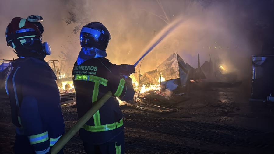 Dos bomberos de la Comunidad de Madrid tratan de apagar un incendio en infraviviendas en Leganés Norte