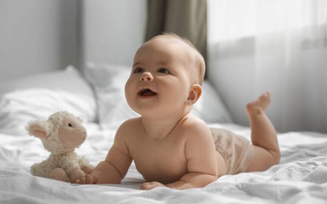 Un bebé sobre la cama con un peluche de una oveja