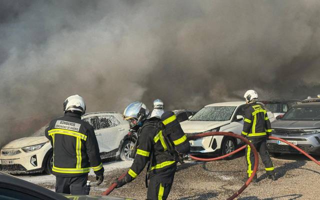 Efectivos de los bomberos tratan de sofocar un incendio que afecta a un aparcamiento con más de 100 vehículos aparcados