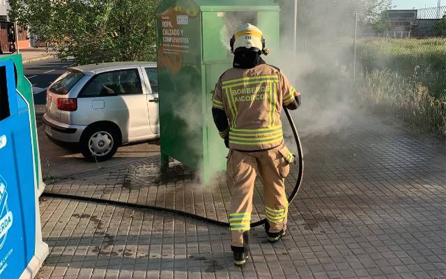 Un bombero apaga el fuego de un contenedor de ropa