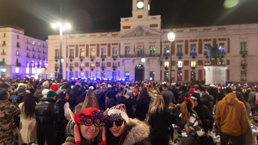 Dos personas disfrazadas se hacen una foto con el reloj de fondo, antes de las campanadas de Nochevieja 2023, en la Puerta del Sol