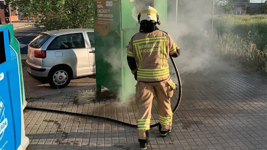 Un bombero apaga el fuego de un contenedor de ropa